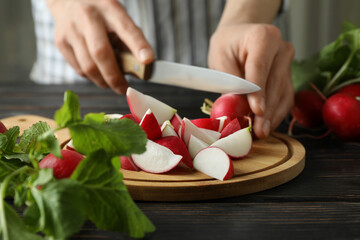 Woman cuts radishes on cutting board on wooden table