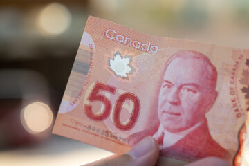 Hand holding a Close up of red Canadian fifty (50) dollar bill of Sir Wilfred Laurier. Defocused...
