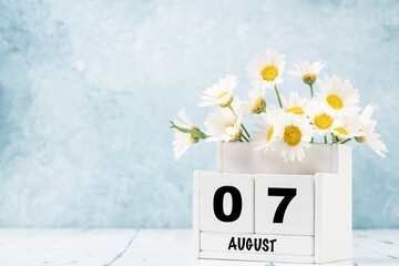 cube calendar for August with daisy flowers over blue