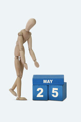 day of the month 25 May calendar . A calendar date on blue cubes and a wooden man standing next to it. White background
