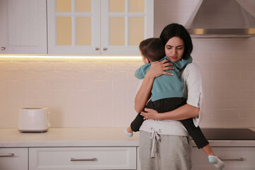 Depressed single mother with child in kitchen, space for text