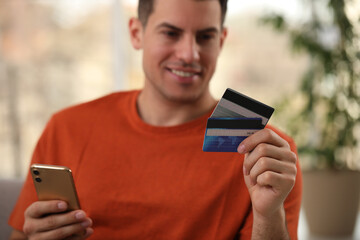 Man using smartphone and credit card for online payment at home