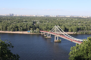 Bridge over the Dnipro river in Kyiv, Ukraine. Panoramic space with green town coastline on a sunny day.