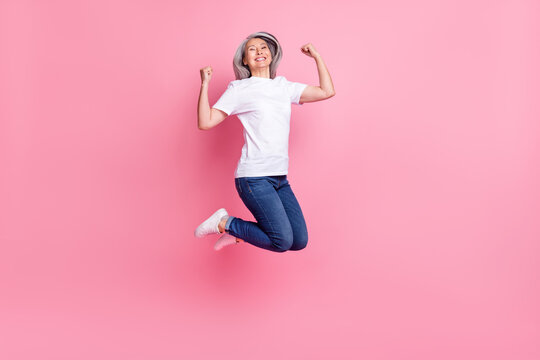 Full length body size photo of elder woman jumping up gesturing like winner overjoyed isolated pastel pink color background