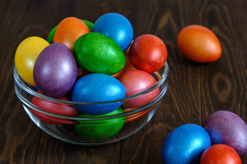 Obraz na płótnie Canvas Colored Easter eggs in bowl of glass on an old wooden table