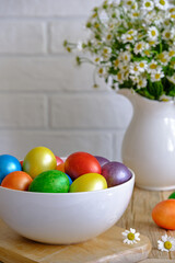 Colored Easter eggs with wild chamomy on old wood table on brick wall background