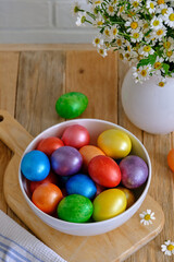 Colored Easter eggs with wild chamomy on old wood table on brick wall background