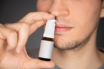 young man use nasal spray and apply the bottle to his nose while pump the medicine to his septum to relieve congestion, itchy and runny nose, and sneezing and make allergies less worse - obrazy, fototapety, plakaty