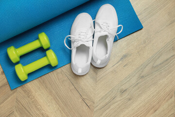 Dumbbells, sneakers and mat on wooden floor, top view. Space for text