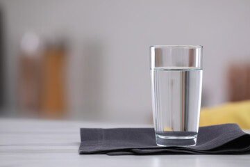 Glass of water and napkin on white table against blurred background. Space for text