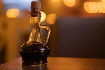 Obraz na płótnie Canvas Curly bottle with handle and wooden cork in glass thin neckwith with balsamic vinegar, oil, sauce in an italian cuisine, cafe, restaurant, warm blurred background. Close-up