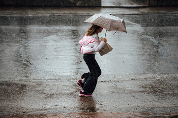 a girl with an umbrella runs through puddles in the rain. wet feet and clothes during a heavy rainstorm. a man escapes from the weather