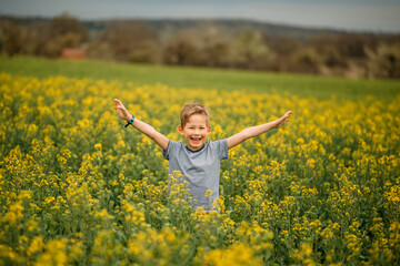 Naklejka na ściany i meble A boy enjoys spring and has fun running in the flowers. He laughs and stretches his hands up.