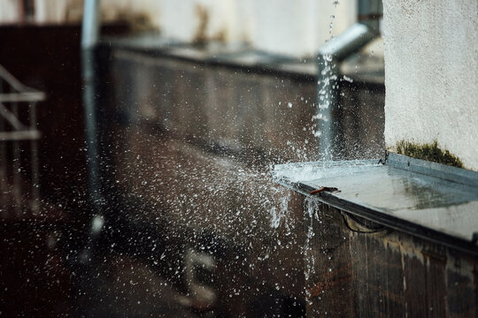 falling raindrops break on the ledge. splashes from running water. drainpipe from the roof of a building during a rainstorm