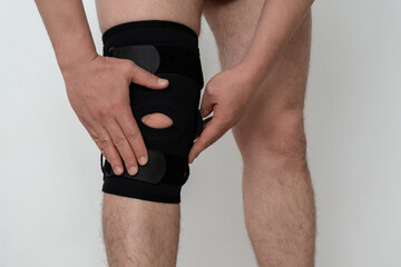 Leg support. A man adjusts a black orthosis on his leg. Copspace