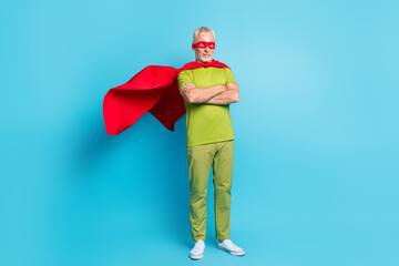 Full length body size view of attractive grey-haired superman folded arms wind blowing isolated over bright blue color background