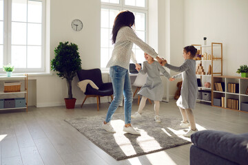 Joyful active happy family having fun enjoy leisure at home. Young mother dancing with daughters children together in living room. Carefree mum with cheerful kids and funny weekend activities
