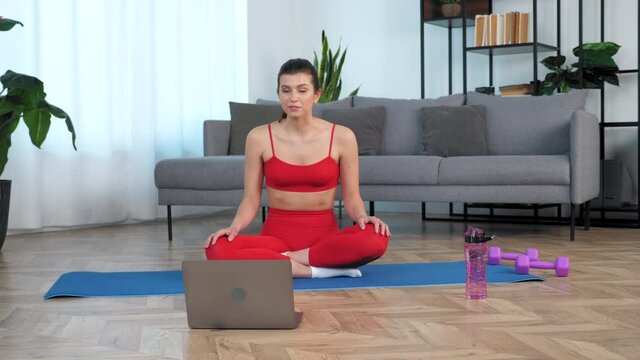 Positive fit woman in sportswear sits on yoga mat talk communicates with fitness trainer, study online remote video conference call webcam chat laptop computer, distance sport education lesson course