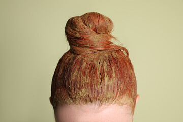 Young woman dyeing her hair with henna on light green background, closeup