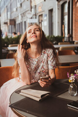 beautiful young girl with long hair is sitting in a cafe and texting on the smartphone