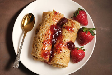 Pancakeshin roll with strawberry jam on plate. Pancakes poured berry jam and decorated fresh strawberries. Top view.