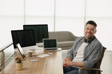 Happy programmer with headphones working at desk in office