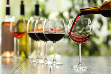 Pouring red wine from bottle into glass on wooden table