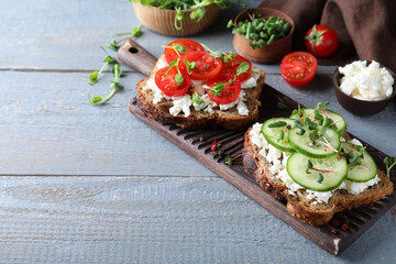 Fototapeta na wymiar Delicious sandwiches with vegetables, cheese and microgreens on grey wooden table. Space for text