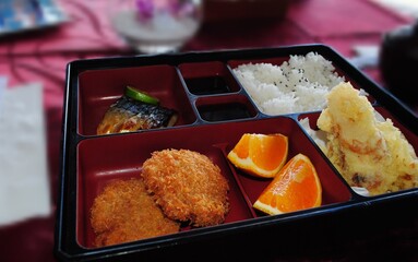 Traditional Japanese bento with portions of rice, breaded chicken, grilled fish and lemon slices.