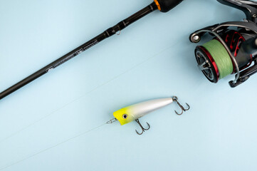 Bass fishing concept on the blue trendy background. Flat lay style. Fishing tackle, popper lure on the line.