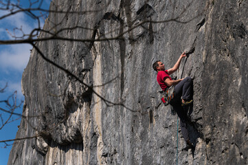 Male climber with red t-shirt and dark pants on limestone rock.