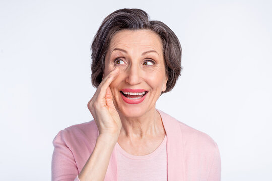 Photo of aged woman happy positive smile whisper tell speak secret look empty space isolated over grey color background