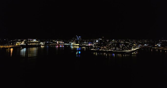 Drone parallax revealing illuminated Opera behind S&oslash;renga pier at night