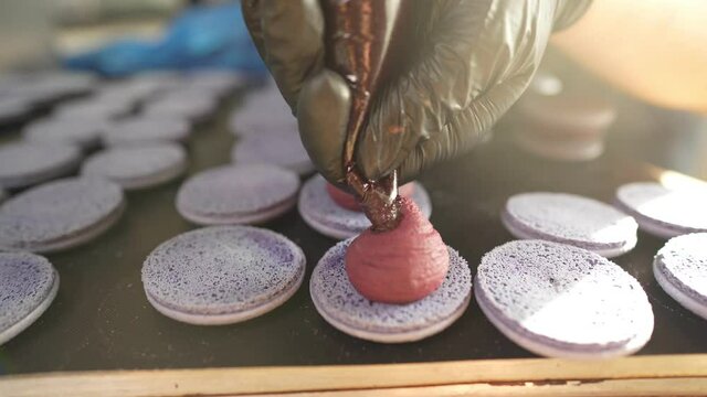 Process Of Making macaroon at home. Shot of hands of female pastry chef holding white macaron with ganache and squeezing red fruit jam from bag. Nature pastry macaroons. High quality 4k footage
