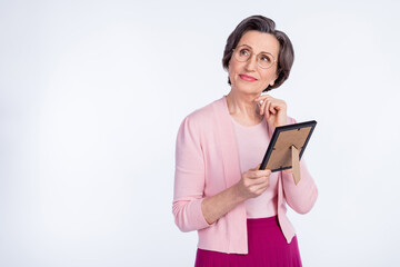 Photo of dreamy cute age woman dressed pink outfit spectacles holding photo frame looking empty space isolated white color background