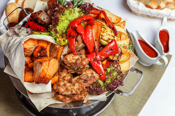 Mixed grill meat, fried vegetables and grilled salmon fish fillets decoration in warm dish