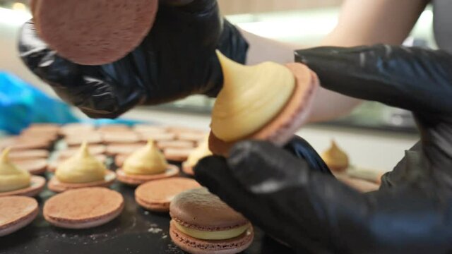 Process Of Making macaroon at home. Shot of hands of female pastry chef holding white macaron with ganache and squeezing red fruit jam from bag. Nature pastry macaroons. High quality 4k footage
