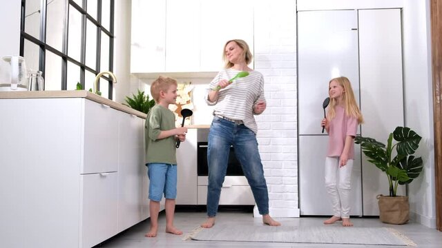 Excited mom or babysiter and two kids boy and girl jumping, dancing laughing in modern scandinavian house kitchen. Happy family mother daughter son having fun enjoy playing singing together at home.
