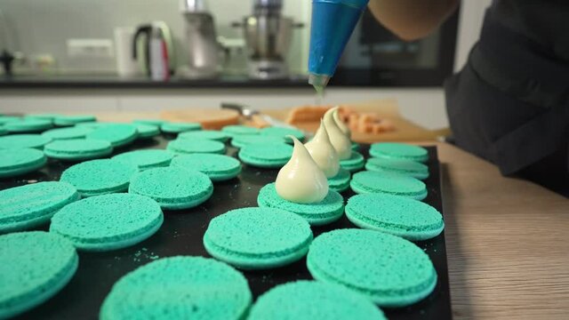 Process Of Making macaroon at home. Shot of hands of female pastry chef holding white macaron with ganache and squeezing red fruit jam from bag. Nature pastry macaroons. High quality 4k footage