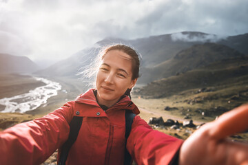 Traveler backpacker young woman taking selfie  on background of mountain in summer cloudy weather.