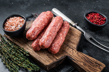 Uncooked Raw beef and lamb meat kebabs sausages on a wooden board. Black background. Top view