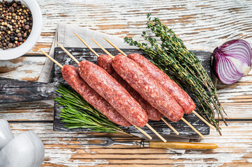 Raw kofta or lula kebabs meat sausages on skewers with herbs. Dark wooden background. Top view