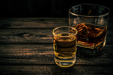 Glass of brandy and tequila on an old wooden table. Angle view, focus on the glass of tequila