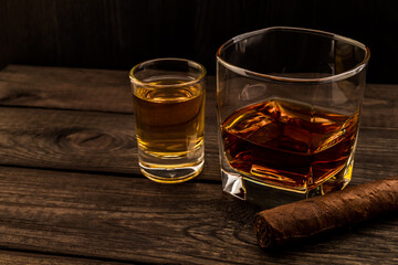 Glass of brandy and tequila with cuban cigar on an old wooden table. Angle view, focus on the cuban cigar