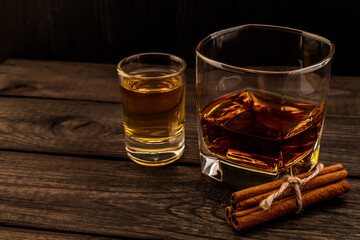 Glass of brandy and tequila with cinnamon sticks tied with jute rope on an old wooden table. Angle view, focus on the cinnamon sticks