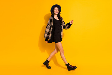Fototapeta na wymiar Photo of pretty young lady walk wear black hat checkered jacket boots isolated yellow color background