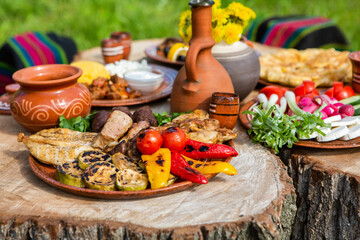 Homemade Romanian Food with grilled meat, polenta and vegetables Platter on camping. Romantic traditional Moldavian food outside on the wood table.