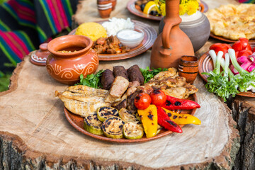 Homemade Romanian Food with grilled meat, polenta and vegetables Platter on camping. Romantic traditional Moldavian food outside on the wood table.
