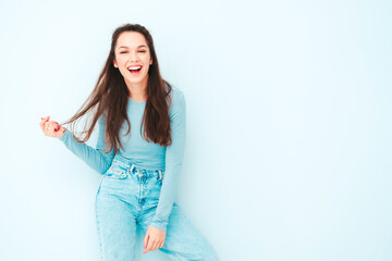 Obraz premium Young beautiful smiling female in trendy summer hipster clothes. Sexy carefree woman posing near light blue wall in studio. Positive model having fun indoors. Cheerful and happy