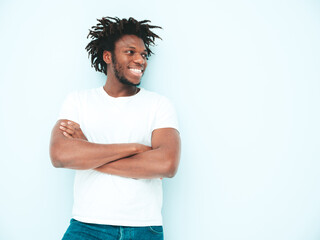 Handsome smiling hipster lambersexual model.Unshaven African man dressed in summer stylish clothes. Fashion male with dreadlocks hairstyle posing near light blue wall in studio.Crossed arms